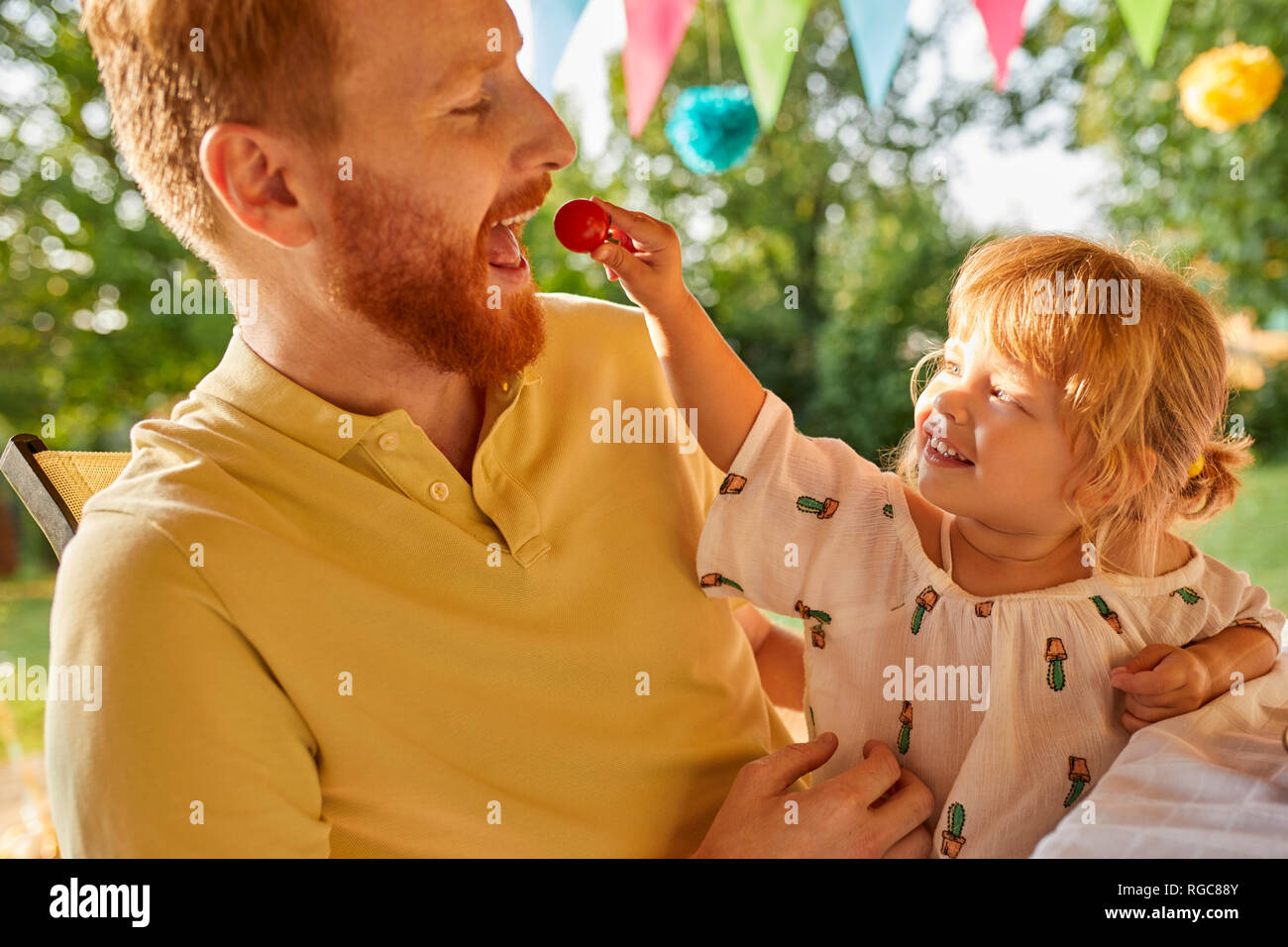 Tochter Fütterung Vater mit Tomaten auf einer Gartenparty Stockfoto