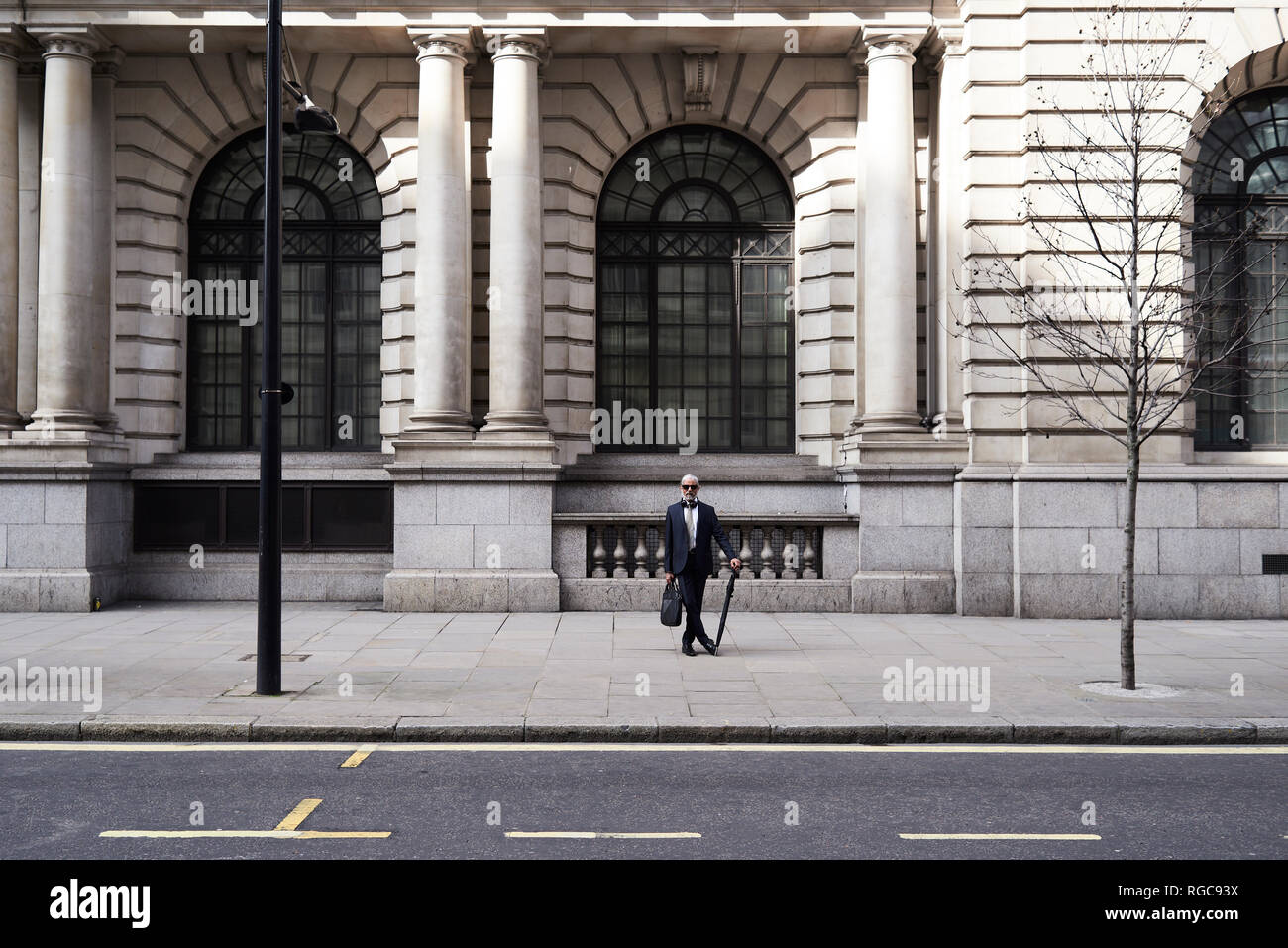 UK, London, stilvollen älteren Geschäftsmann mit Tasche und Schirm stehen auf Pflaster Stockfoto