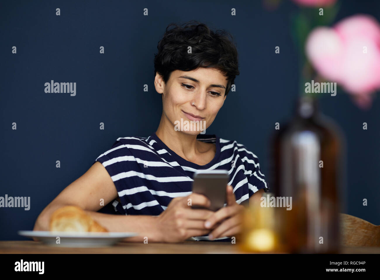 Lächelnde Frau zu Hause an den hölzernen Tisch Handy prüfen. Stockfoto