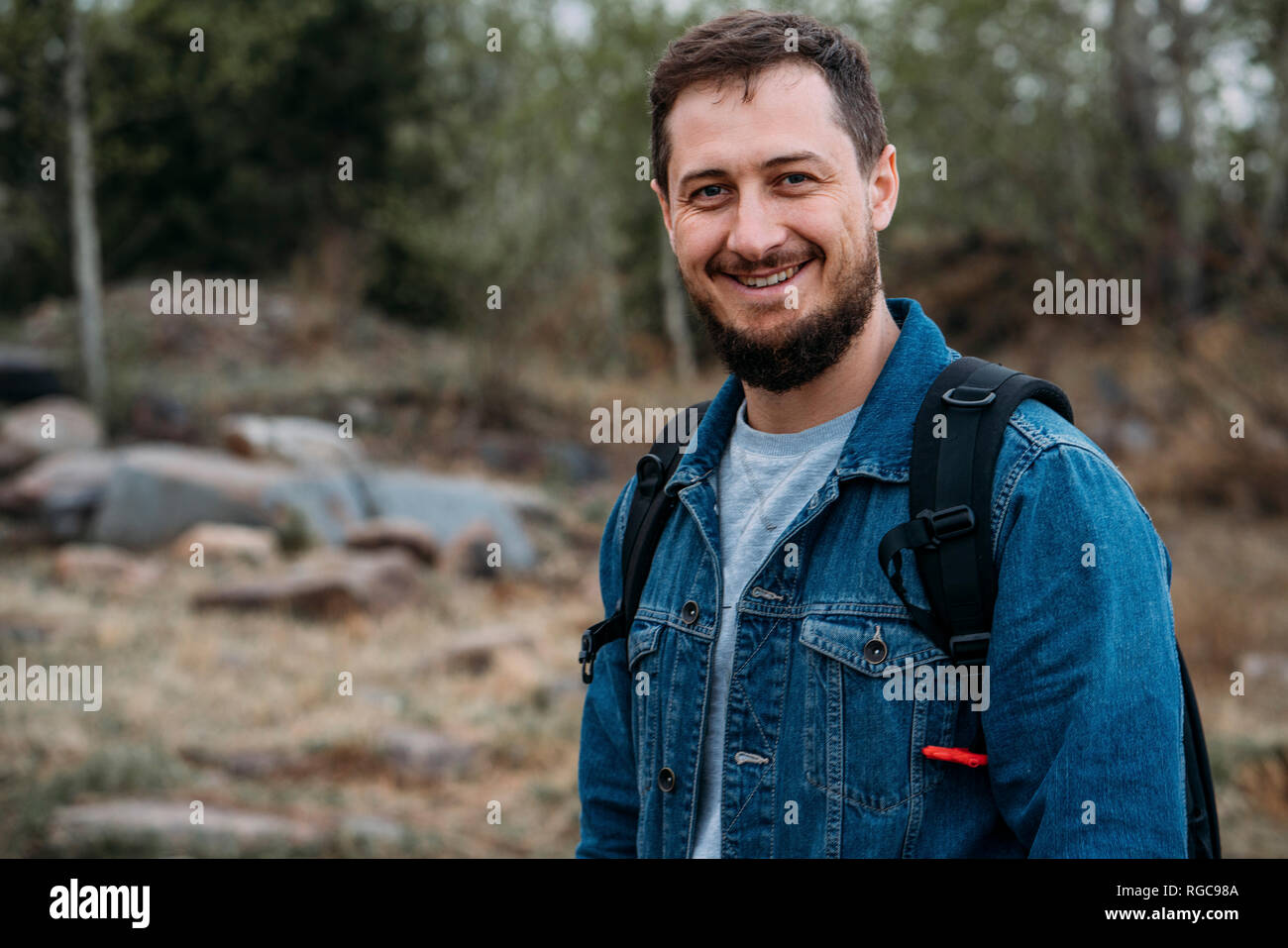 Portrait von lächelnden Mann mit Rucksack tragen Jeans Jacke in der Natur Stockfoto