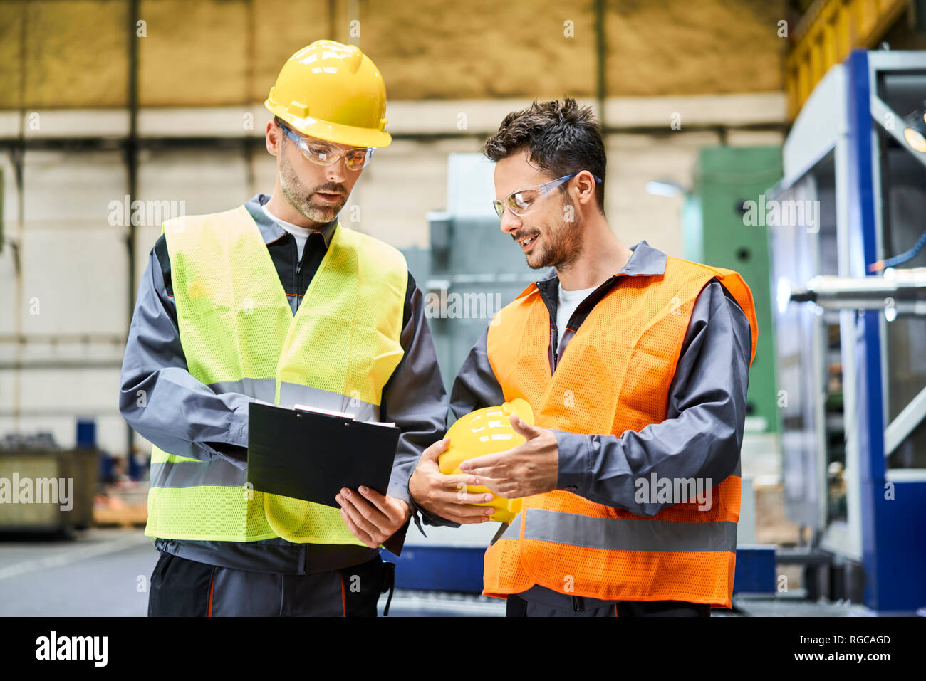 Zwei Männer tragen von Arbeitskleidung holding Zwischenablage und sprechen in der Factory Stockfoto