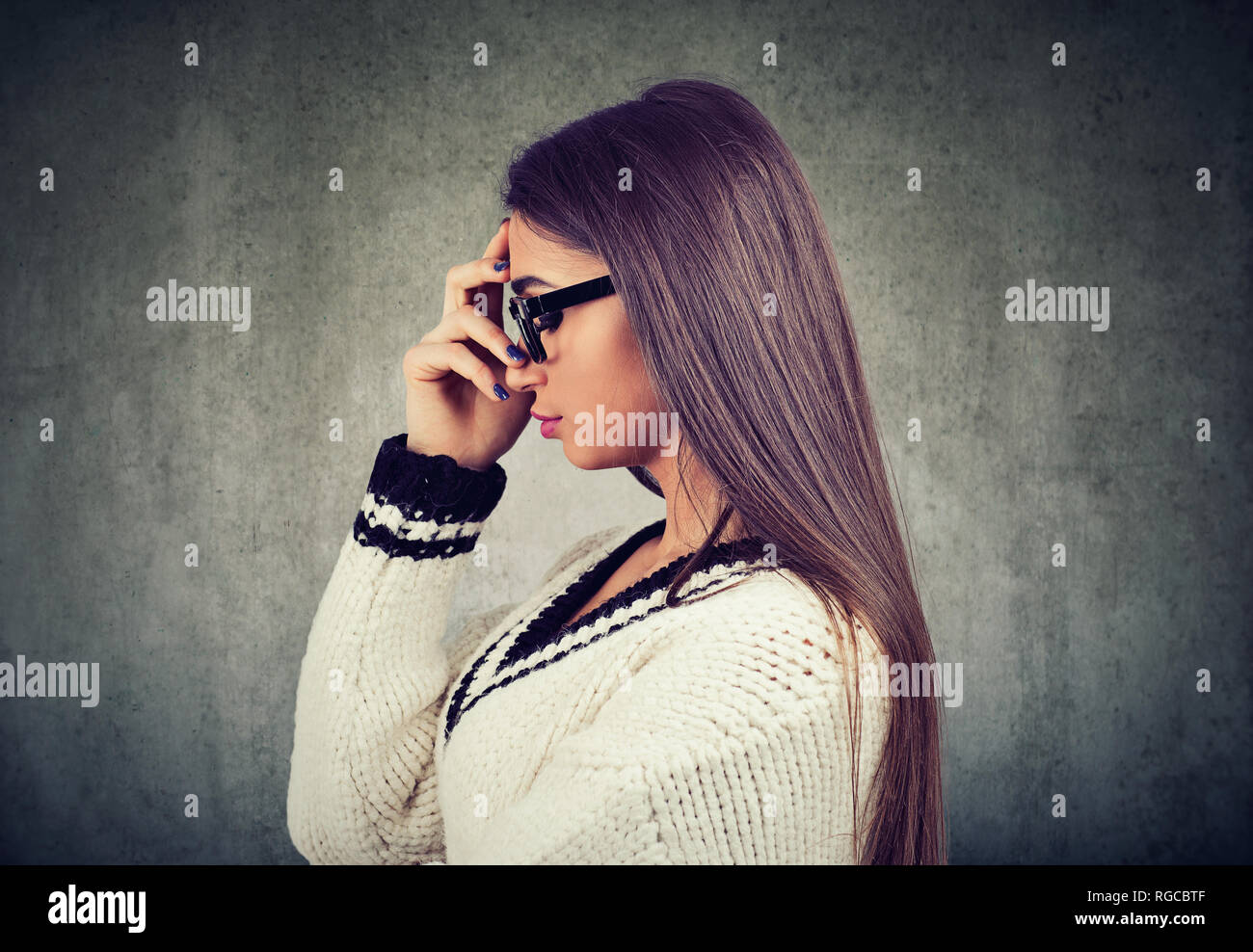 Seitenansicht der junge Brünette in Gläsern die Hand auf die Stirn in Achtsamkeit auf grauem Hintergrund Stockfoto