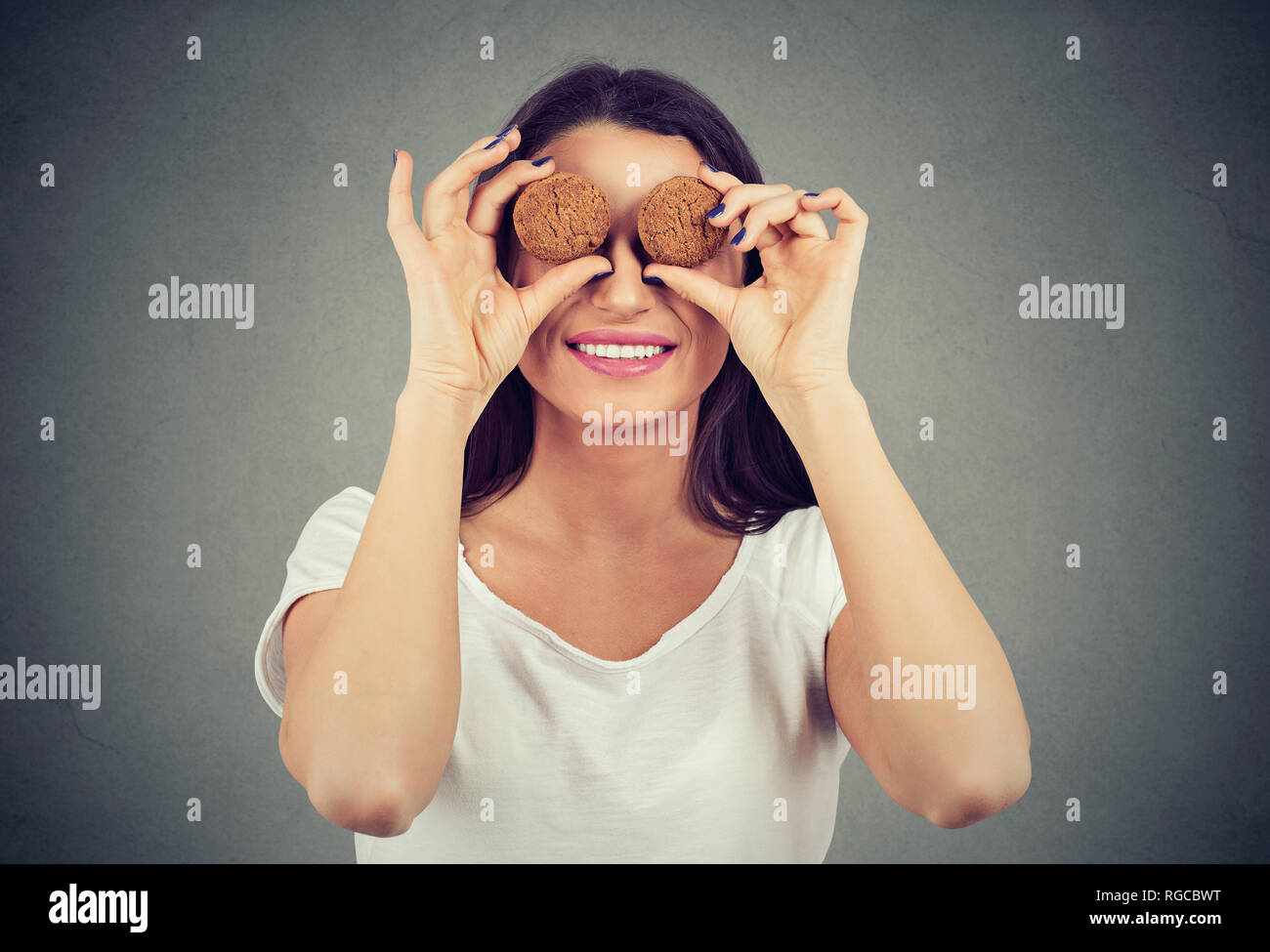 Nette junge Frau mit Cookies der vor ihren Augen und glücklich lächelnd Stockfoto