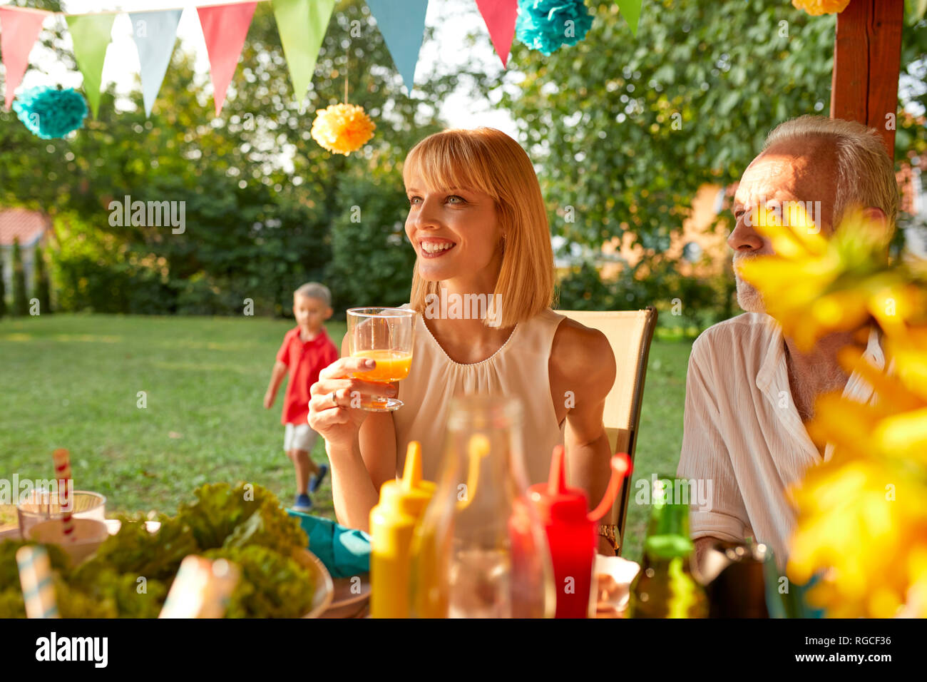Lächelnde Frau trinkt Orangensaft auf einer Gartenparty Stockfoto
