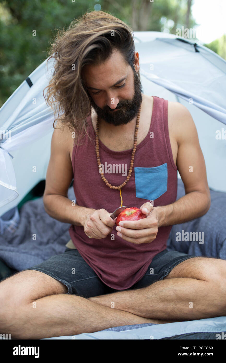 Mann vor einem Zelt Peeling ein Apple sitzen Stockfoto