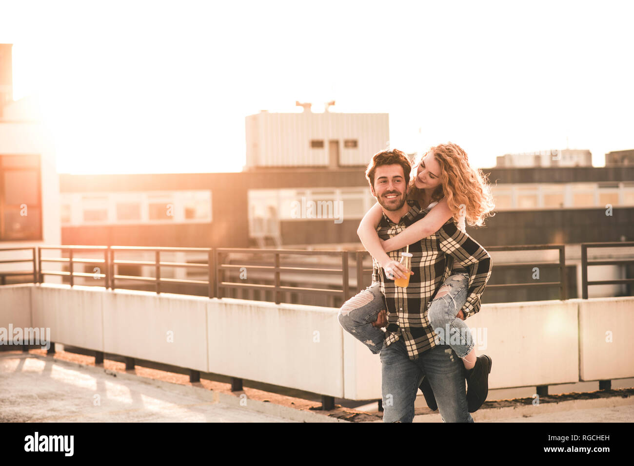 Portrait des jungen Mannes, seiner Freundin ein piggyback Ride auf dem Dach Terrasse bei Sonnenuntergang, Stockfoto