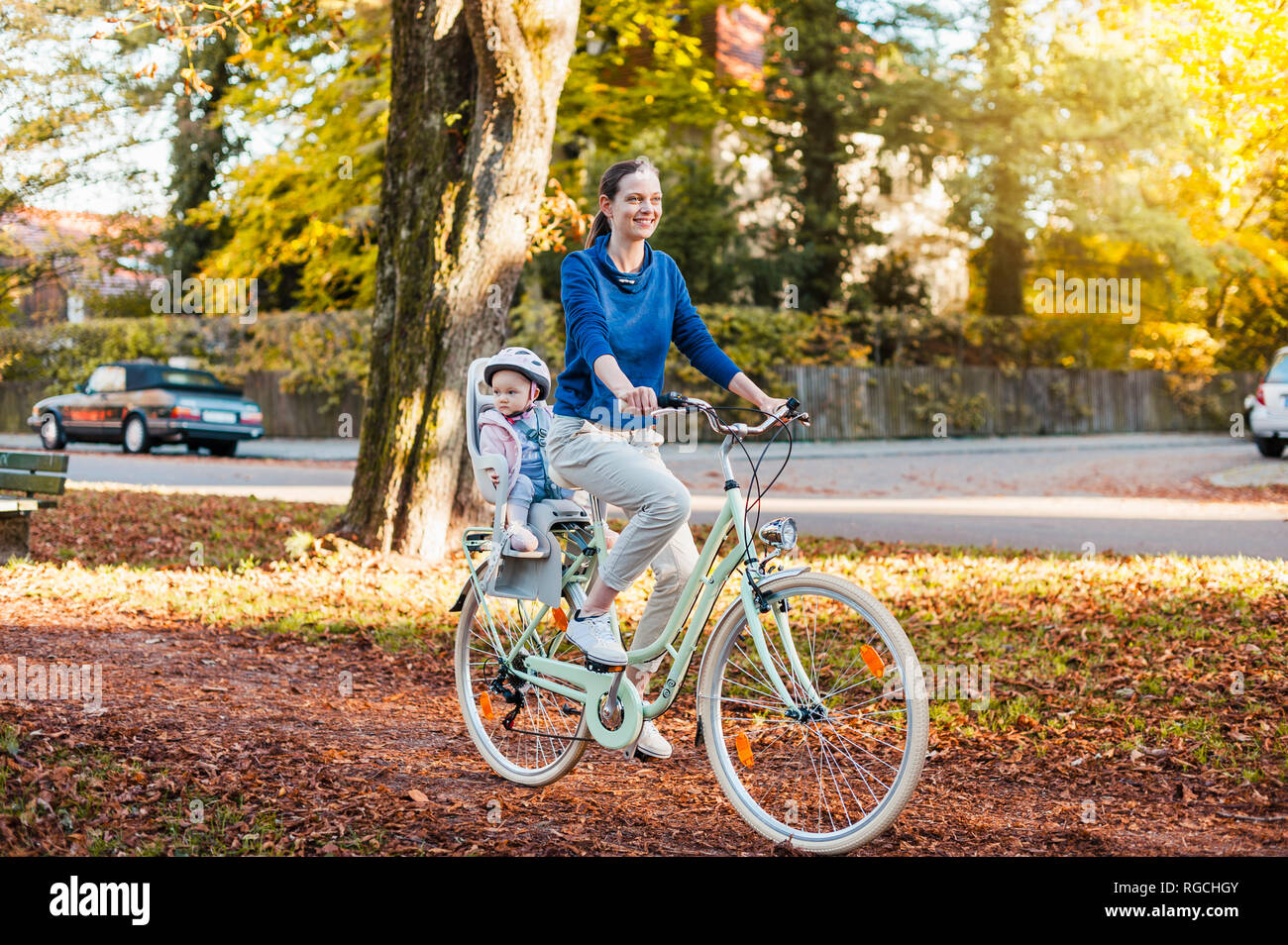 Mutter und Tochter Reiten Fahrrad, Baby tragen Helm im Kindersitz sitzen Stockfoto