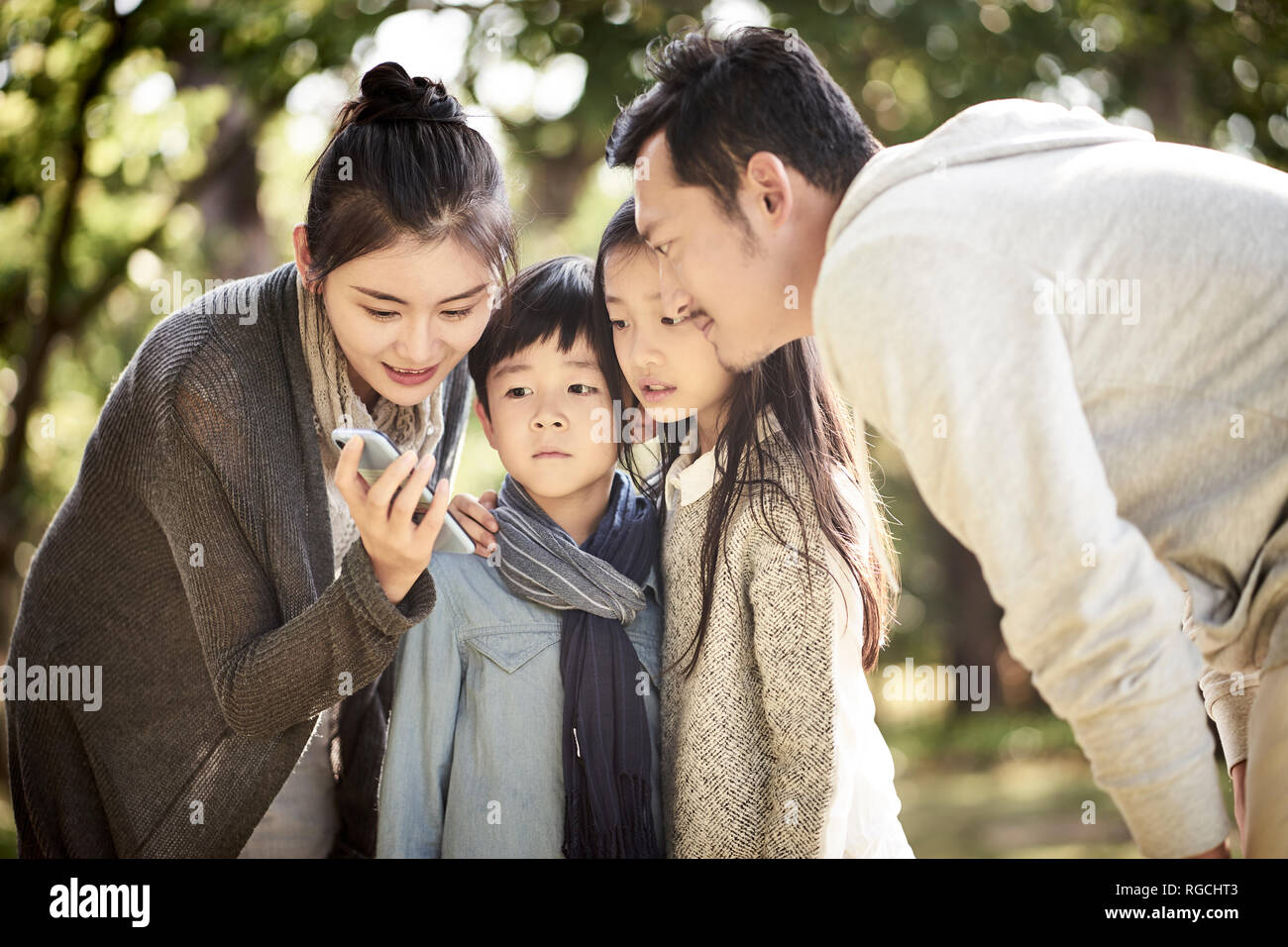 Asiatische Familie Eltern und zwei Kinder an Handy suchen gemeinsam in einem Park. Stockfoto