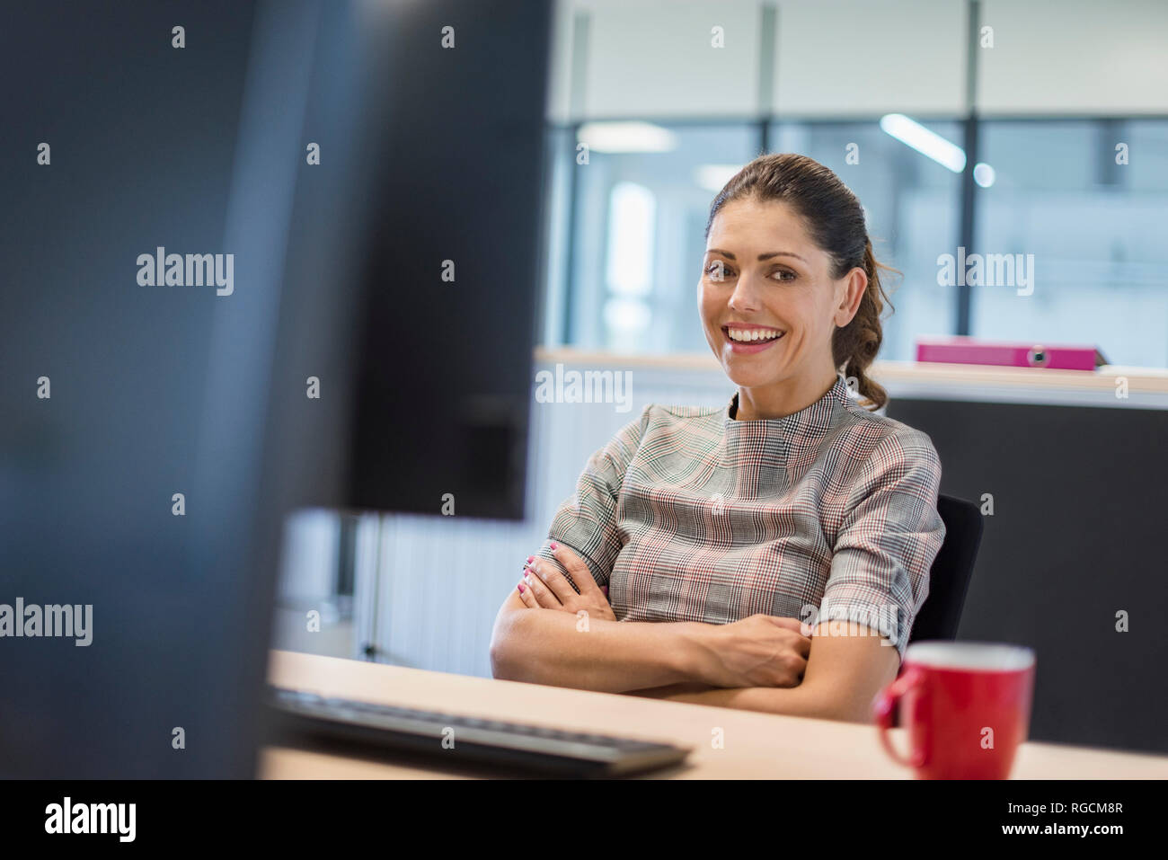 Weibliche Büroangestellte am Schreibtisch sitzen, mit verschränkten Armen Stockfoto