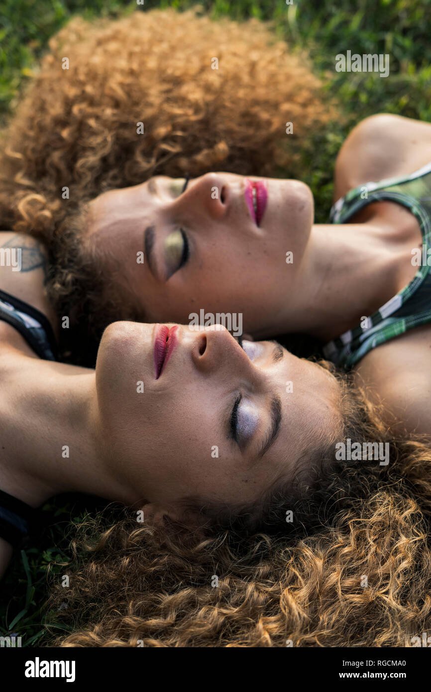 Portrait von rouged Zwillingsschwestern Seite an Seite liegen auf einer Wiese Stockfoto
