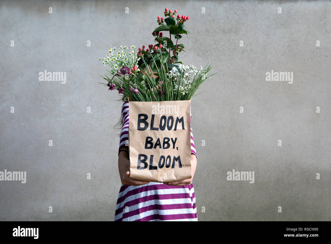 Mädchen versteckt sich hinter Papiertüte mit Blumen Stockfoto
