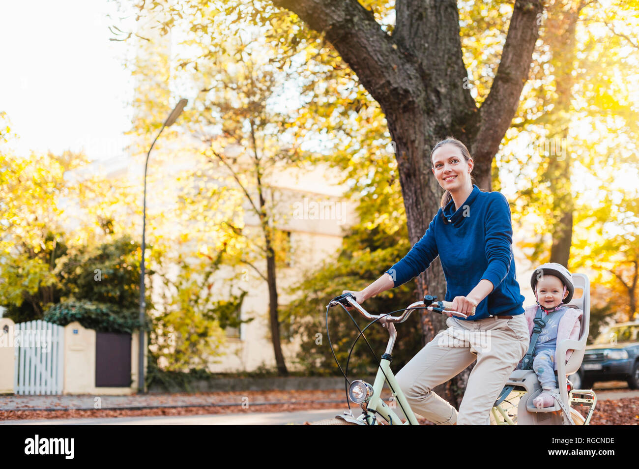 Mutter und Tochter Reiten Fahrrad, Baby tragen Helm im Kindersitz sitzen Stockfoto
