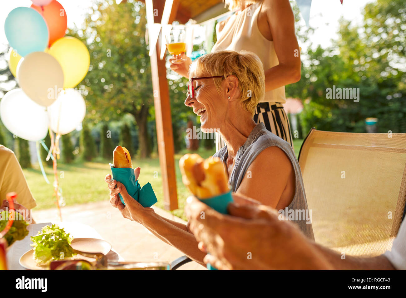 Glückliche Frau essen einen heißen Hund auf einer Gartenparty Stockfoto