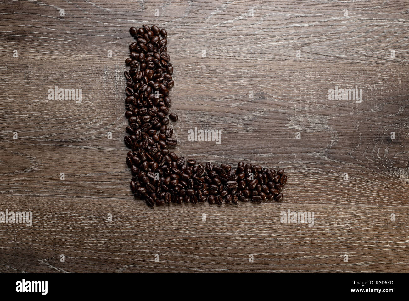Dunkel geröstete Kaffeebohne auf einem Holztisch in der Form von Text Buchstaben L angeordnet Stockfoto