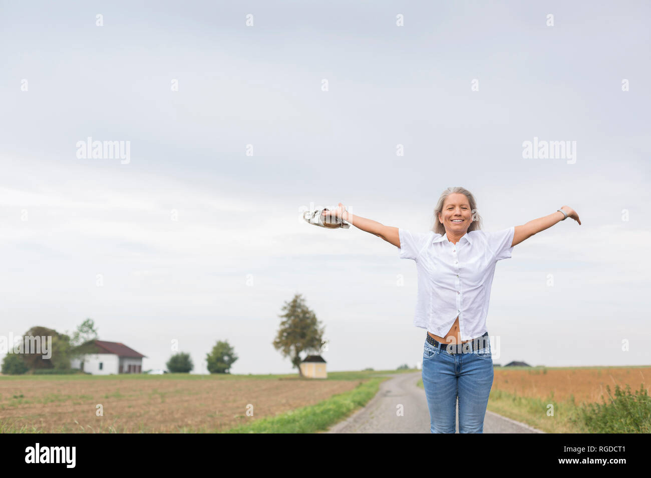 Reife Frau steht auf Remote country lane im Sommer mit ausgestreckten Armen Stockfoto