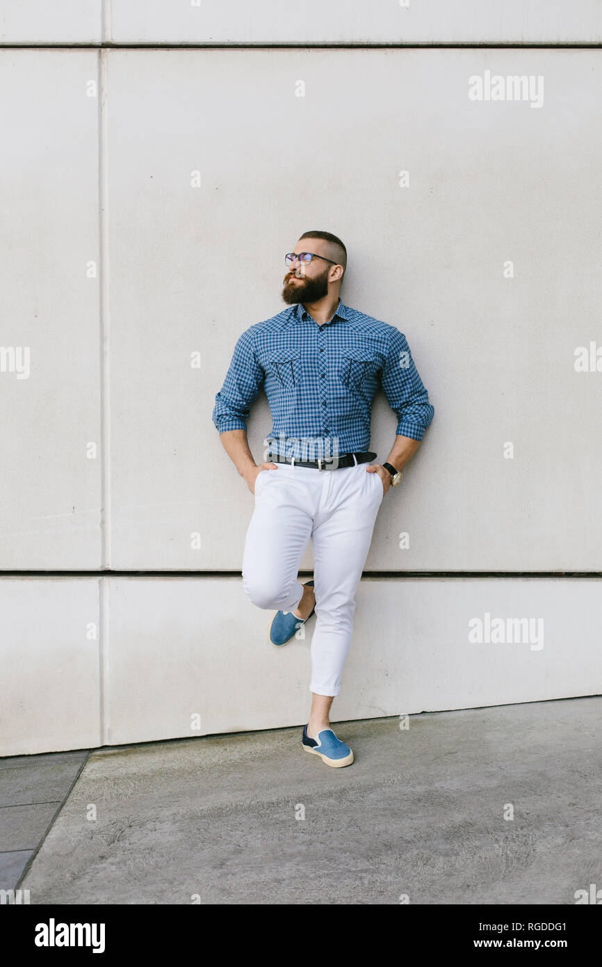 Bärtige hipster Geschäftsmann Brillen und Plaid Shirt gegen die Wand lehnt Stockfoto