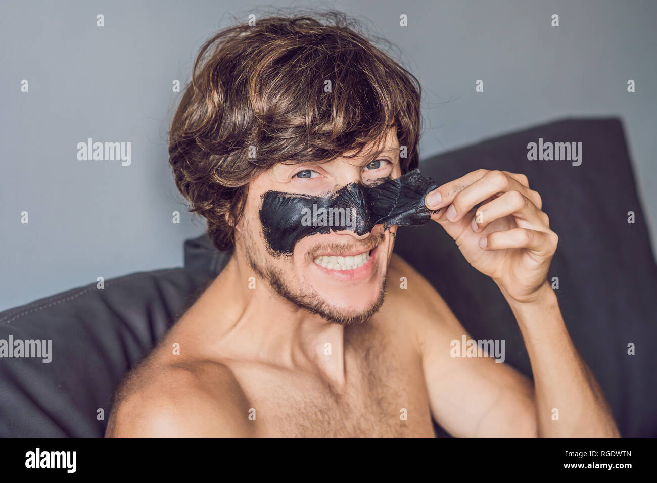 Glückliche Menschen mit schwarzer Maske auf dem Gesicht. Foto Mann empfangen von Wellnessanwendungen. Beauty Skin Care Concept Stockfoto