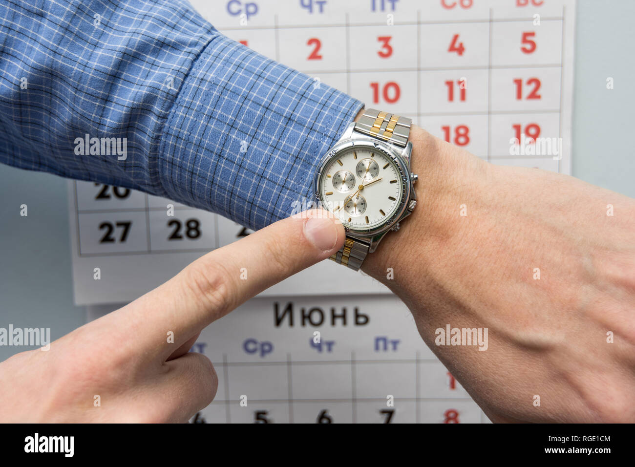 Hand Office Specialist zu einer Armbanduhr, und im Hintergrund ist ein Wandkalender Stockfoto