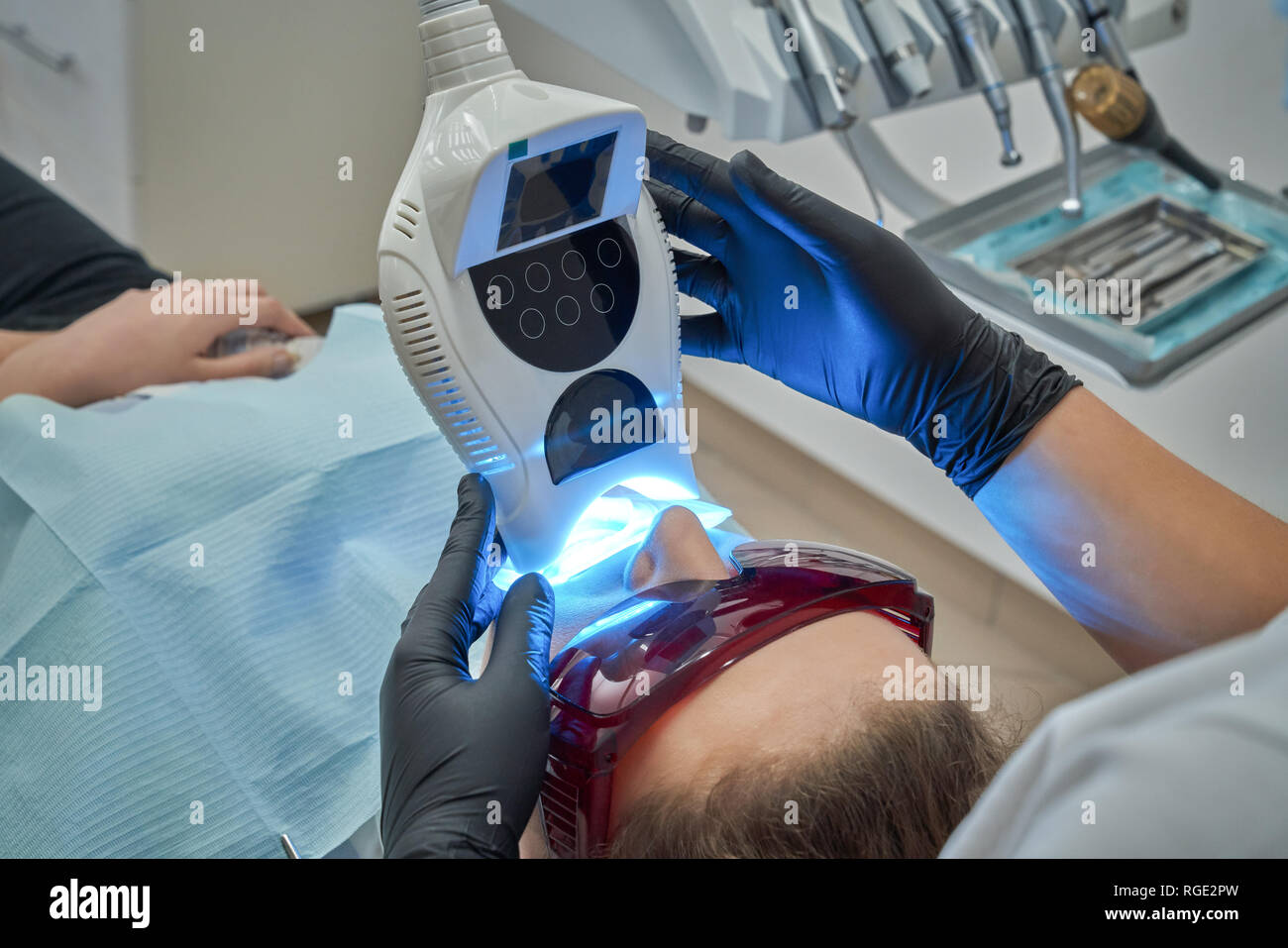 Verfahren der Zähne, die in der Zahnheilkunde Klinik. Frau bekleidet in Schutzbrille liegen auf zahnarztstuhl. Arzt halten moderne Gerät, UV-Lampe mit blauem Licht, Stockfoto