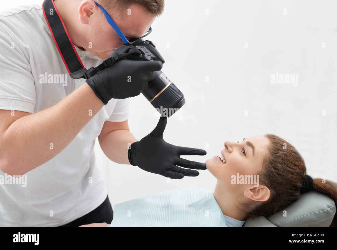 Wunderschöne Frau liegend auf Zahnarztstuhl und posieren. Adorable, schöne Frau, Zähne und strahlendes Lächeln nach Zahnmedizin Pflege. Fotograf in schwarz Handschuhe mit Foto. Stockfoto
