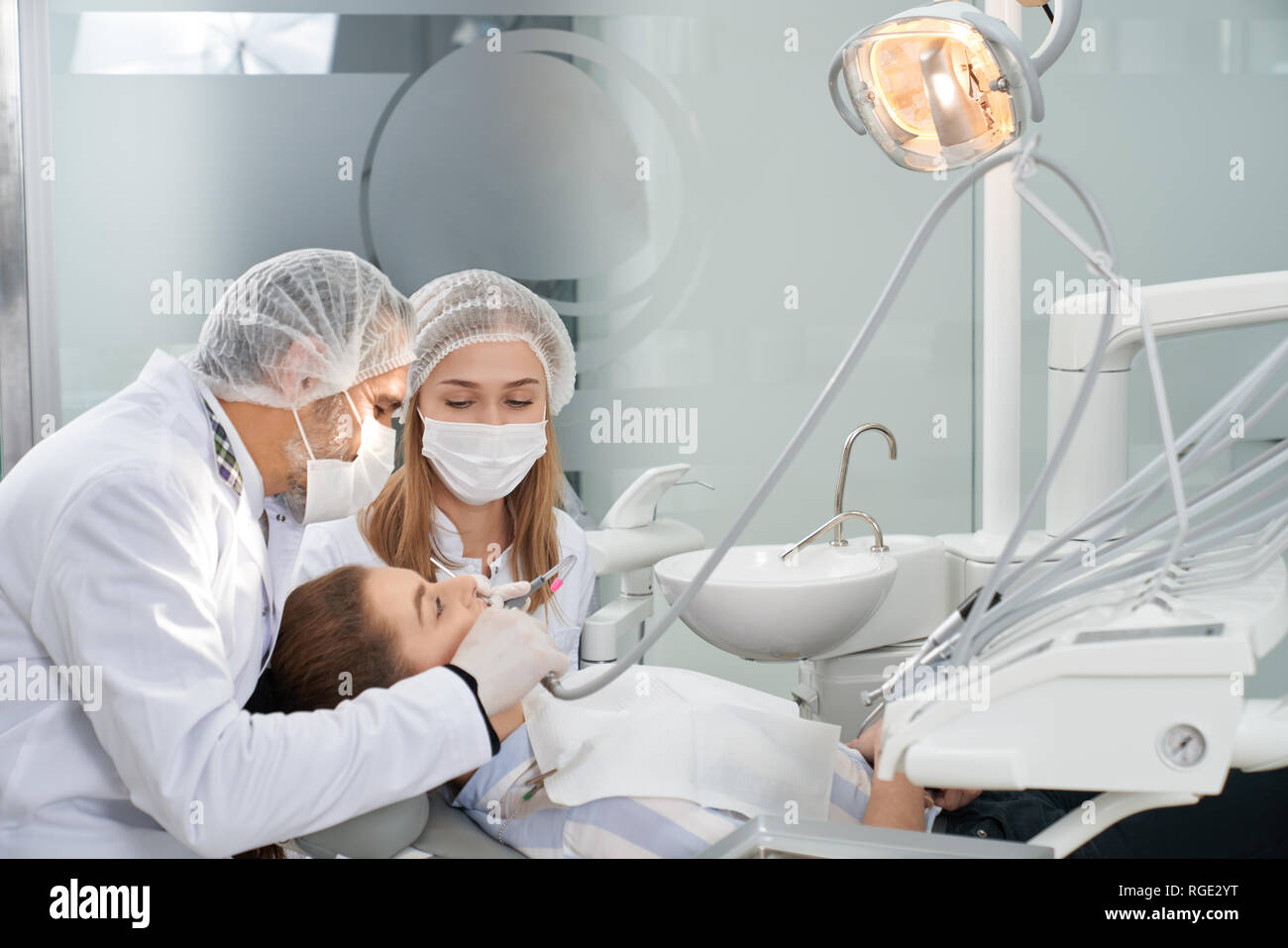 Der modernen Zahnmedizin Privatklinik mit professioneller Ausstattung. Zahnärzte arbeiten mit den Zähnen von Client. Liegende Frau auf Zahnarzt cahir. Ärzte tragen in der medizinischen Caps, Formung und Masken. Stockfoto