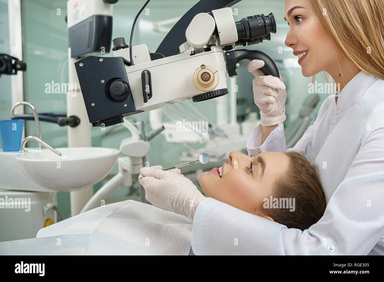 Seitenansicht der jungen Frau liegend auf zahnmedizinischen Stuhl während des Verfahrens in der Klinik. Professionelle weiblichen Zahnarzt Kontrolle der Zähne mit modernen Mikroskop. Konzept der Zahntechnik und Zahnmedizin. Stockfoto