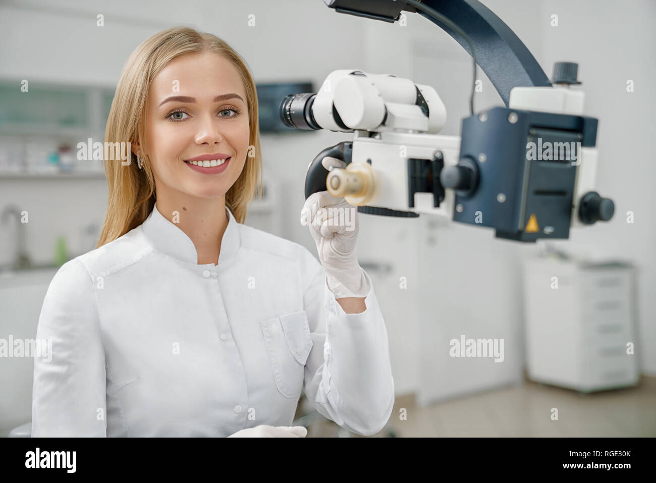 Vorderansicht des schönen weiblichen Zahnarzt in weiße Uniform an Kamera suchen und lächelnd. Junger Arzt sitzen Arbeiten in Zahnarztpraxis und moderner Ausstattung. Konzept der Stomatologie. Stockfoto