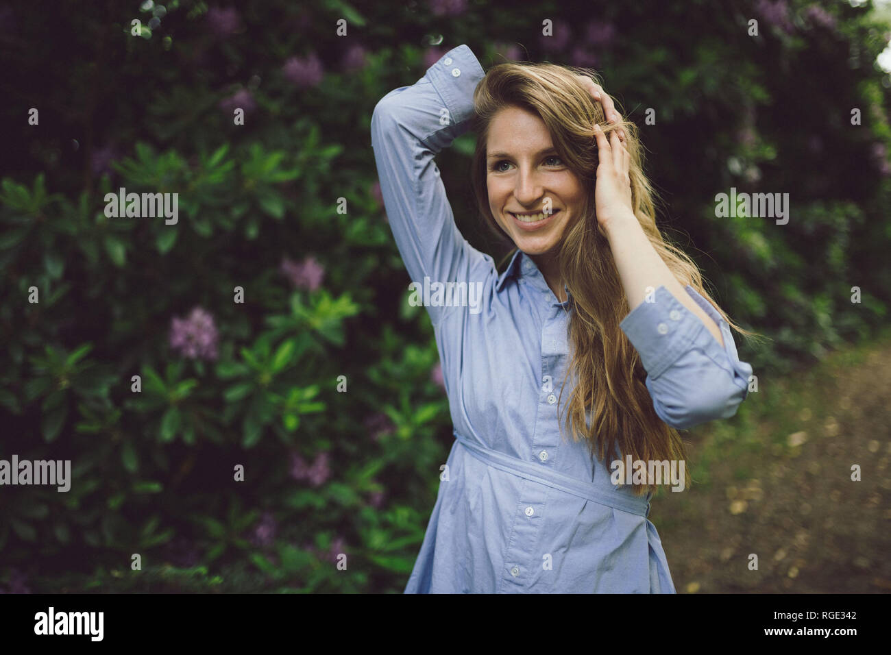 Schöne junge Mädchen in einem blauen Kleid Gehen durch einen Park, spielen mit ihren langen blonden Haaren, glücklichen Ausdruck im Gesicht Stockfoto