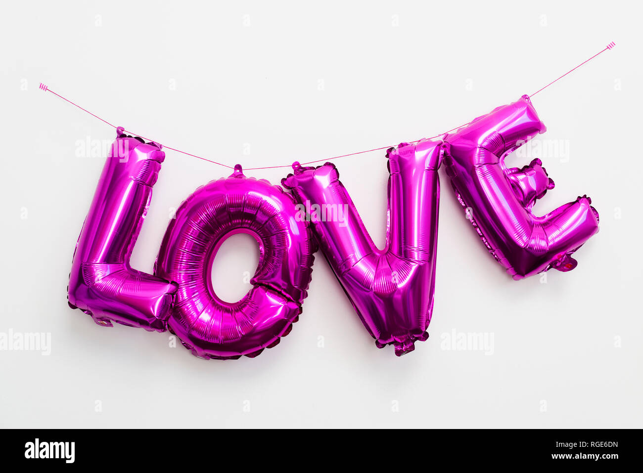 Einige fuchsia Brief-förmige Ballons, die das Wort Liebe, hängend an einer weißen Wand Stockfoto