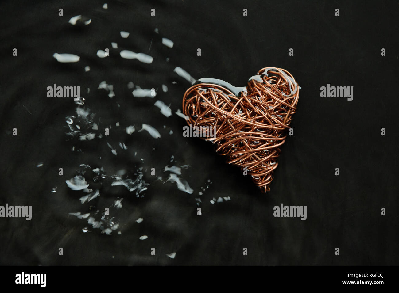 Kupferdraht Herzen aus wiedergewonnenem elektrische Kabel. In Wasser, dessen Oberfläche durch Tröpfchen gestört wurde, Stockfoto