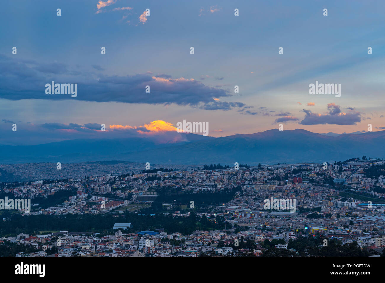 Stadtbild von Quito während der Blauen Stunde bei Sonnenuntergang mit dem Höhepunkt der Cayambe Vulkan bei Sonnenuntergang in den Anden, Ecuador beleuchtet. Stockfoto