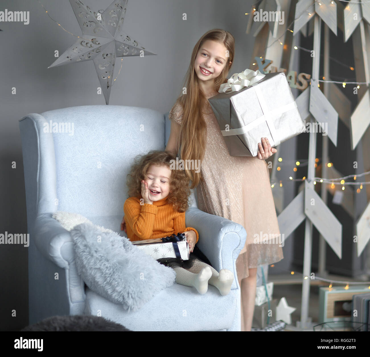 Zwei kleine Mädchen mit Geschenken steht in der Nähe eine stilisierte Weihnachtsbaum Stockfoto