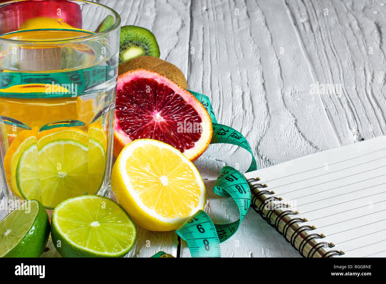 Fitness Concept mit Früchten und detox Wasser. Fitness Motivation mit Zentimeter- und Notebook auf weißem Holz- Hintergrund. Nach oben Schließen Stockfoto