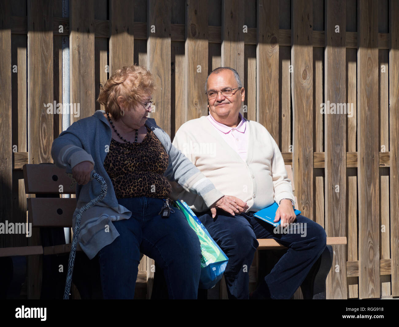 Ein älteres Paar auf einer Bank sitzen. Der Mann lächelt angenehm an der Frau, wie sie für seine Hand reicht. Schuss an der Texas State Aquarium. Stockfoto