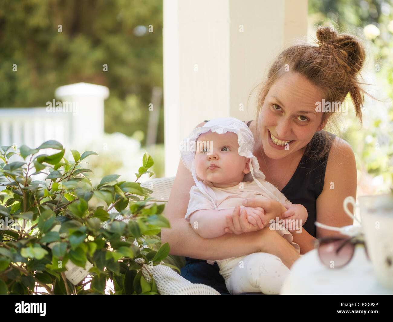 Portrait von lächelnden Mutter mit Baby auf dem Schoß sitzen auf der Terrasse Stockfoto