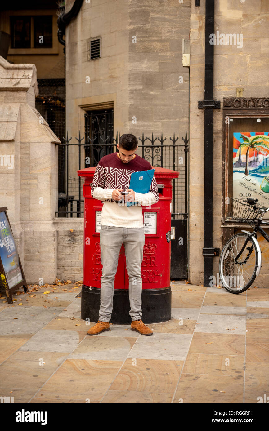 Männlicher Student, der SMS auf seinem Handy an der roten Postfächer in Oxford, Oxfordshire, Großbritannien, schickt Stockfoto
