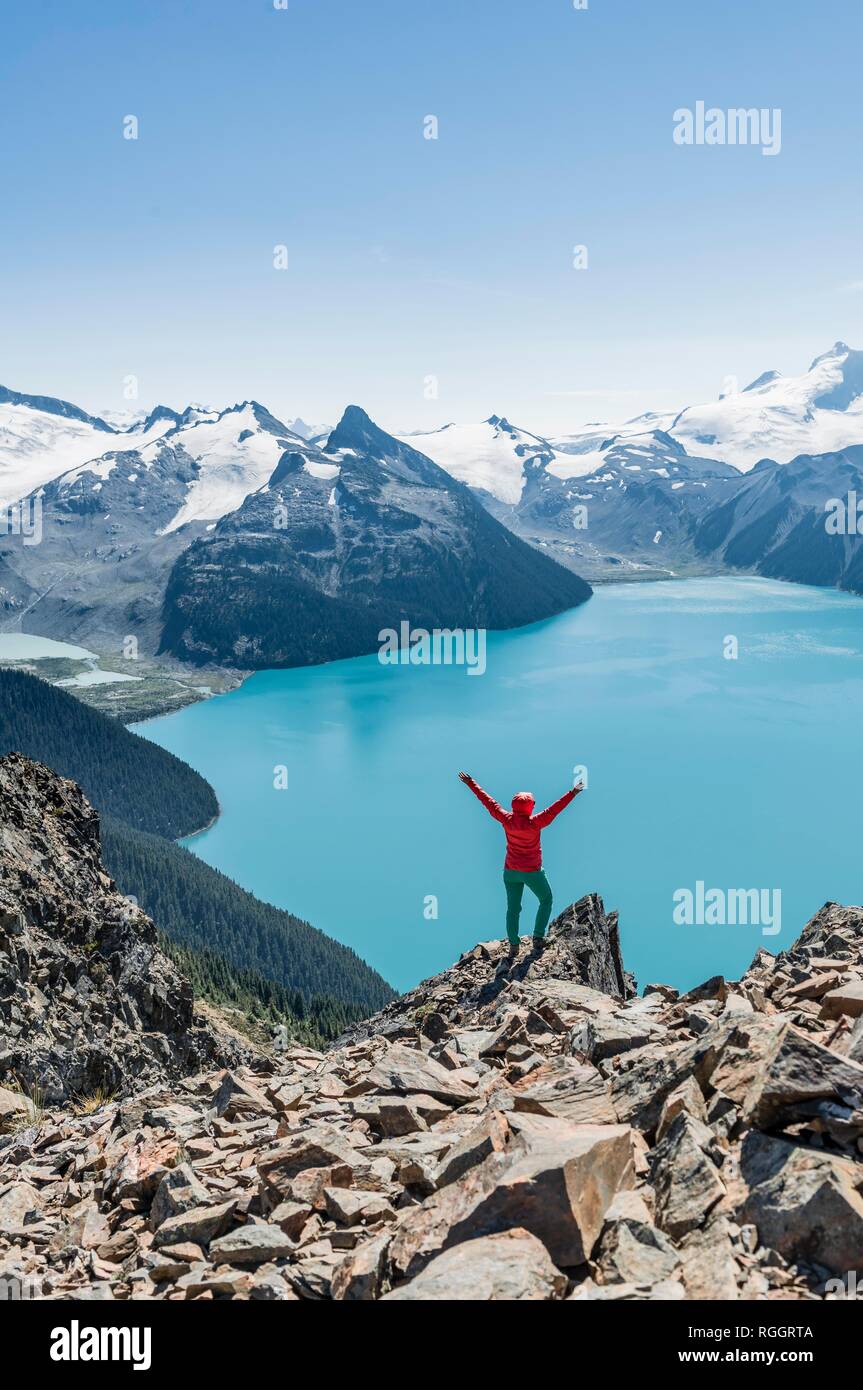 Blick vom Panorama Ridge Wanderweg, Wanderer auf einem Felsen streckt die Arme in die Luft, See, Garibaldi Guard Berg und Stockfoto