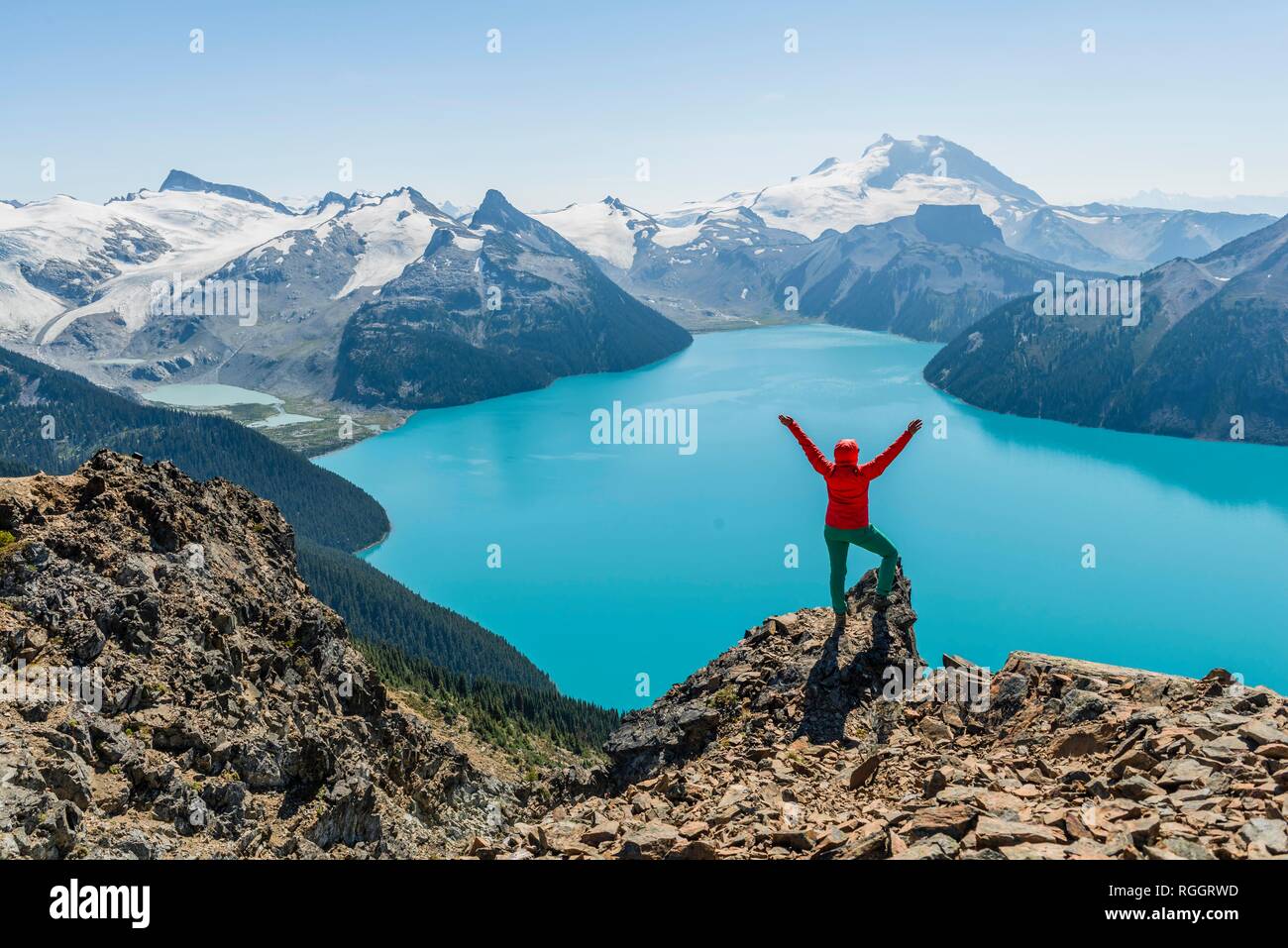Blick vom Panorama Ridge Wanderweg, Wanderer auf einem Felsen streckt die Arme in die Luft, See, Garibaldi Guard Berg und Stockfoto