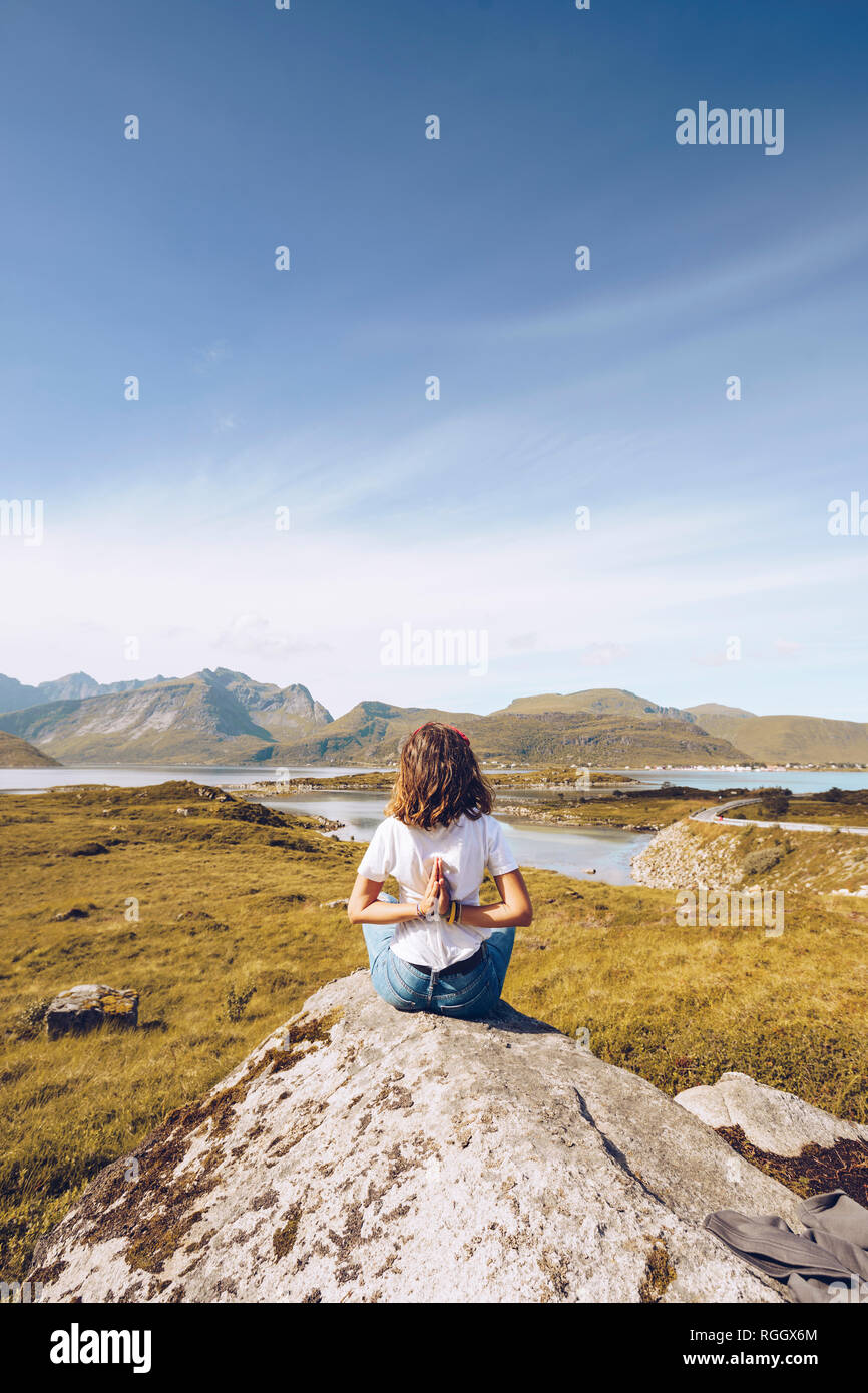 Norwegen, Lofoten, Rückansicht der jungen Frau sitzt auf einem Felsen Yoga Übung Stockfoto