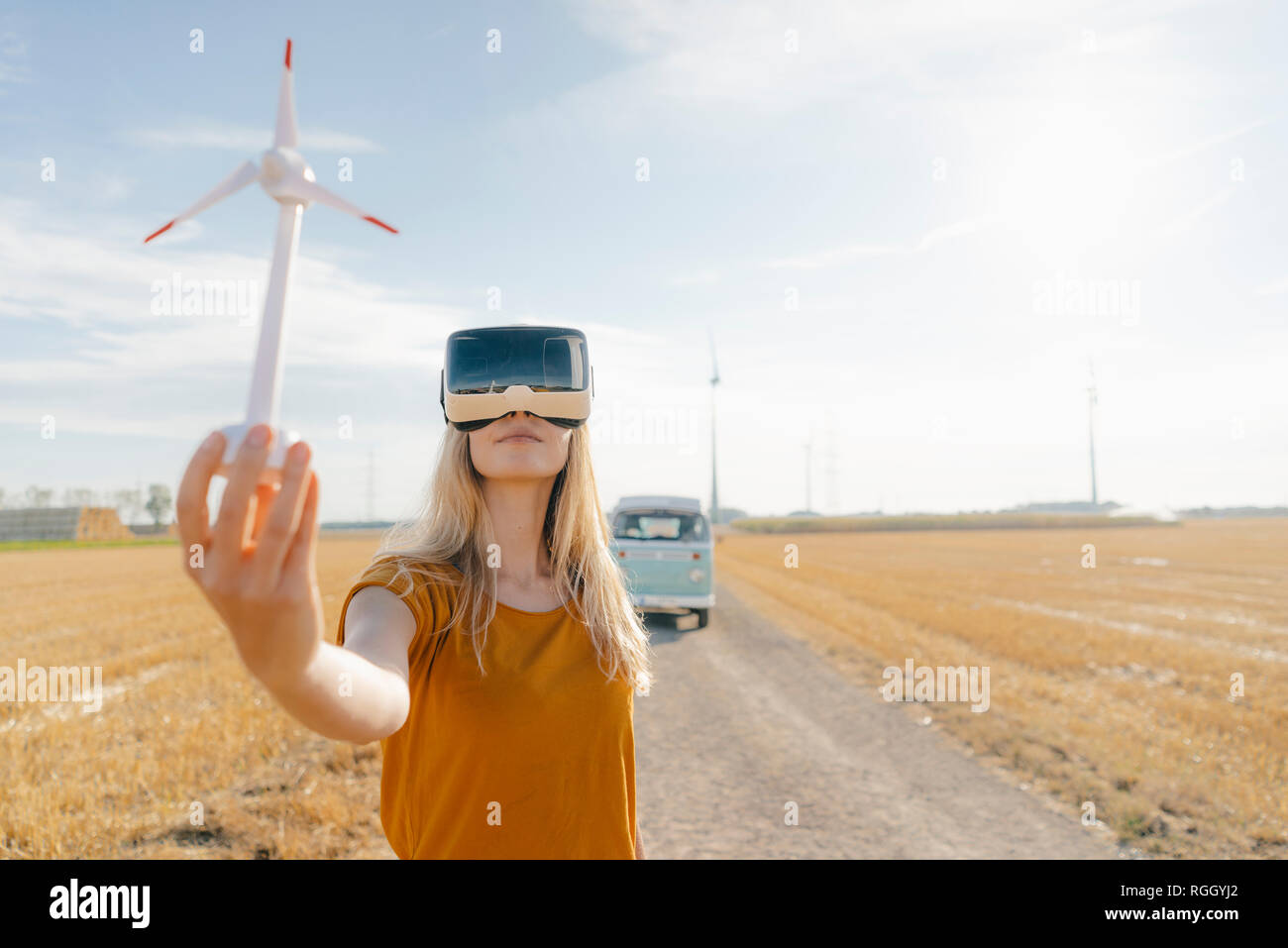 Junge Frau mit VR-Brille im Wohnmobil in ländlichen Landschaft Holding wind turbine Modell Stockfoto