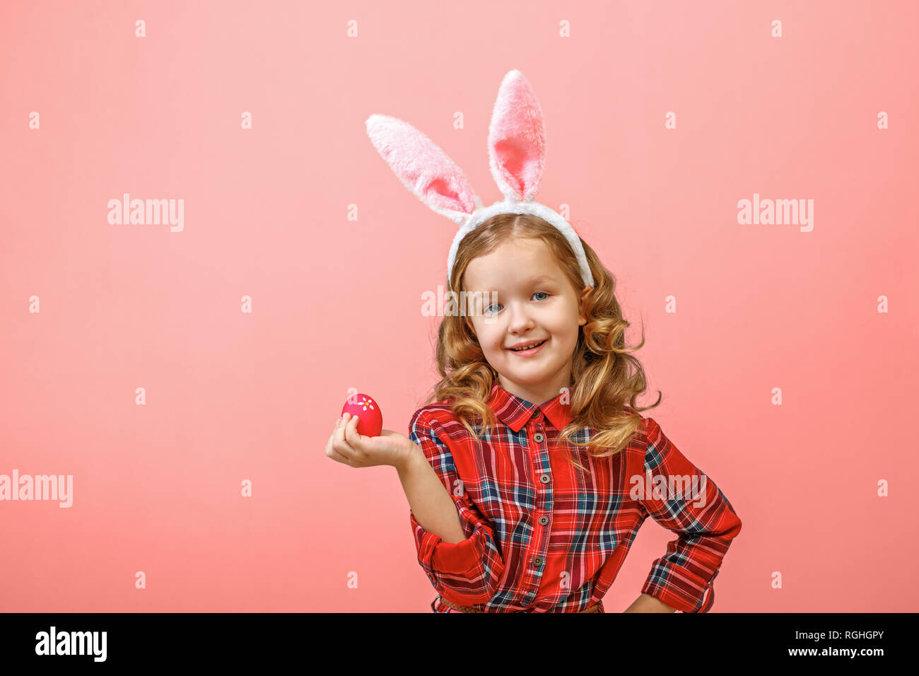 Fröhliche kleine Kind Mädchen mit Hasenohren mit einem Osterei auf einen farbigen Hintergrund. Stockfoto