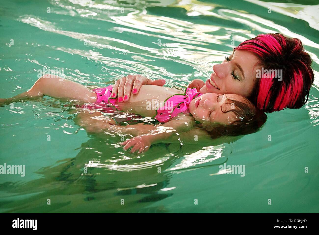 Mutter mit junger Tochter lernt, wie sie im häuslichen Pool mit gefärbten Haaren auf Mama schwimmen kann, die von Kleinkindern als vertrauenswürdig angesehen wird Stockfoto