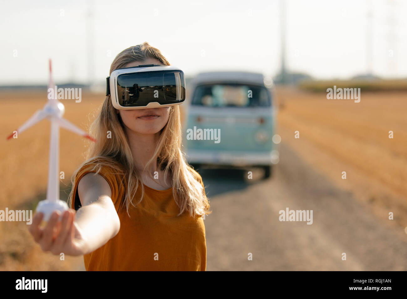 Junge Frau mit VR-Brille im Wohnmobil in ländlichen Landschaft Holding wind turbine Modell Stockfoto