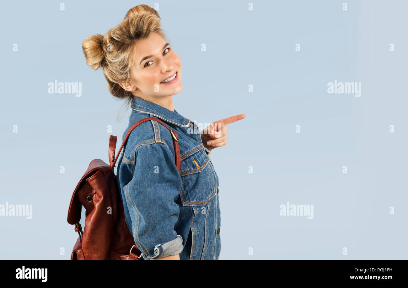 Gerne schöne Schüler Mädchen in einer Jeansjacke mit einem Rucksack auf den Schultern im Studio auf einem blauen Hintergrund. Der Begriff der Bildung und Lernen Stockfoto