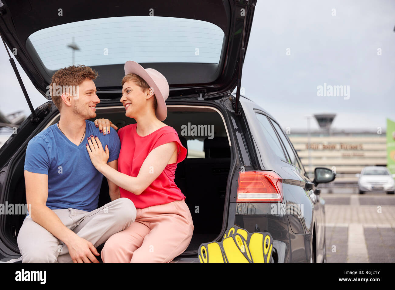 Glückliches junges Paar im Kofferraum am Flughafen sitzen Stockfoto