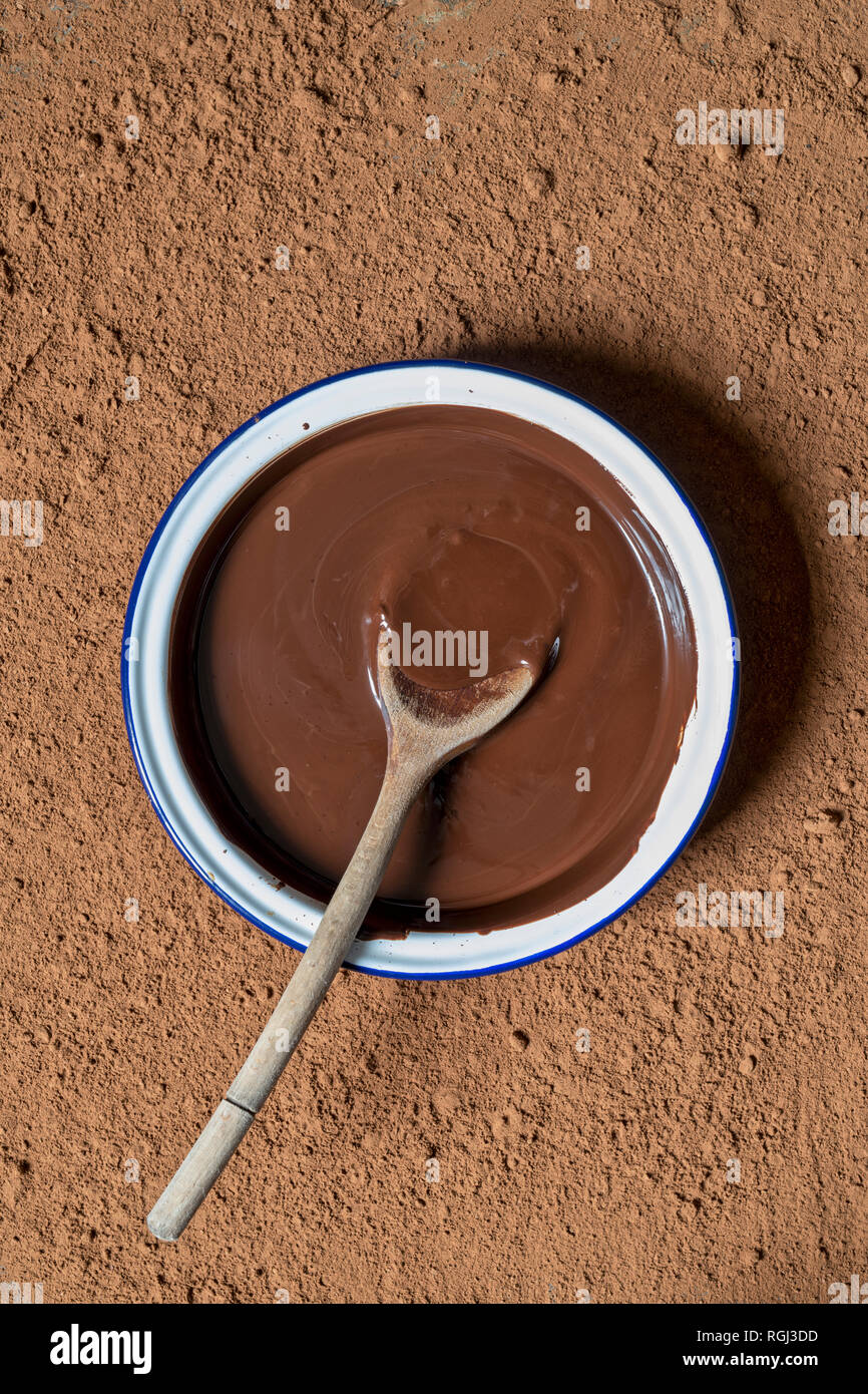 Geschmolzene Schokolade und Löffel aus Holz in eine Schüssel von Kakaopulver umgeben Stockfoto