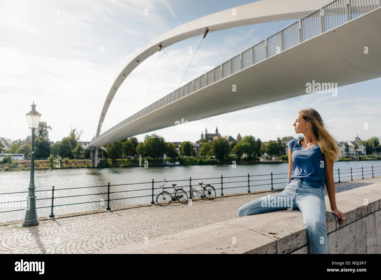 Niederlande, Maastricht, junge Frau sitzt auf einer Wand am Flußufer Stockfoto