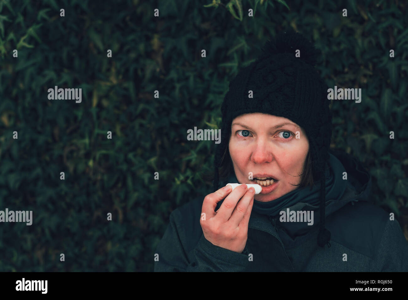 Frau Anwendung Lip Balm auf der Straße an einem kalten Wintertag gegen den gemeinsamen Efeu an der Wand Stockfoto