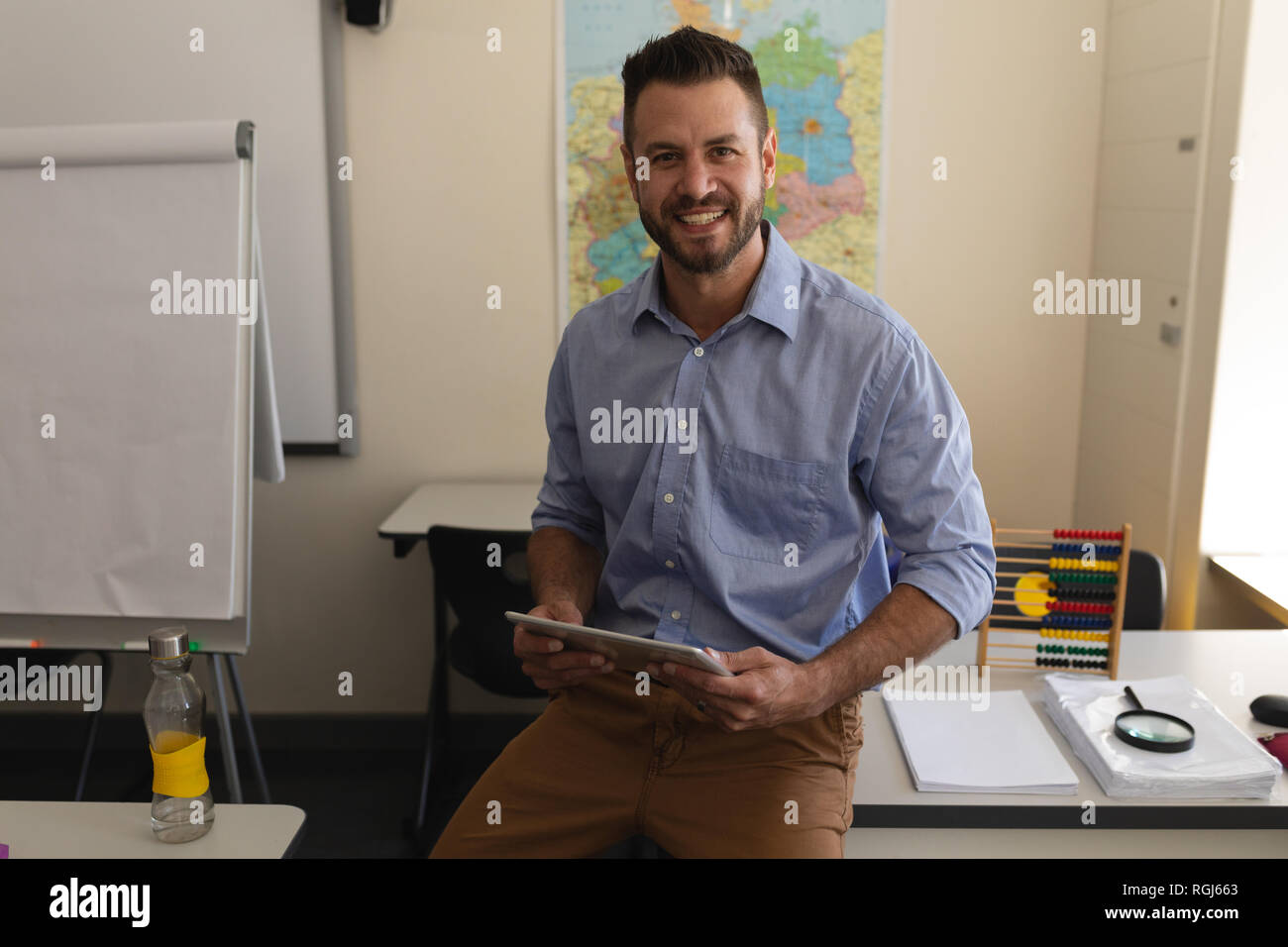 Schule Lehrer An Kamera Und Sitzen Am Schreibtisch Im Klassenzimmer Stockfotografie Alamy