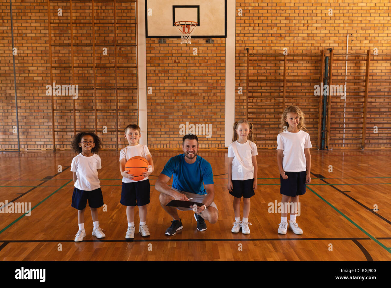 Gerne Basketball Trainer und schoolkids an Kamera am Basketballplatz suchen Stockfoto
